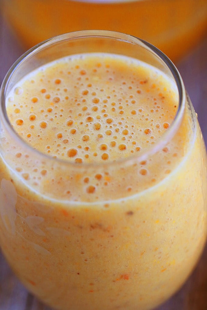 A close up of the top of a glass of orange Julius with bubbles 