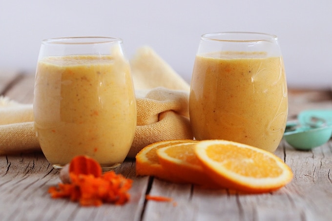 Two glasses of orange Julius on a table with fresh orange and turmeric root