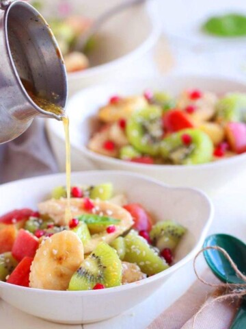 A close up someone pouring dressing on a bowl of fruit salad