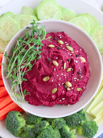 roasted beet hummus in a white bowl surrounded by fresh vegetables