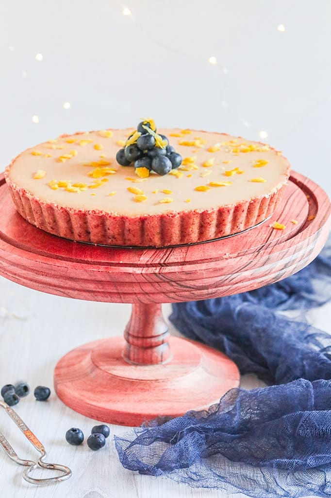 A lemon cheesecake sitting on a wooden cake stand on a white table