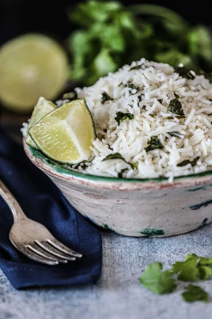 ceramic bowl of rice topped with cilantro and lime on gray table top