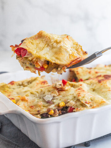 person scooping a slice of vegan enchilada casserole out of a white dish