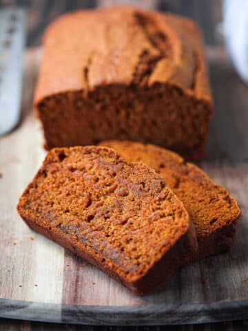 2 slices of pumpkin bread on wood cutting board with rest of loaf in background