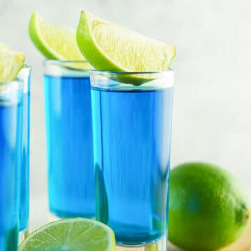 side view of blue kamikaze shot in a shot glass with wedge of lime