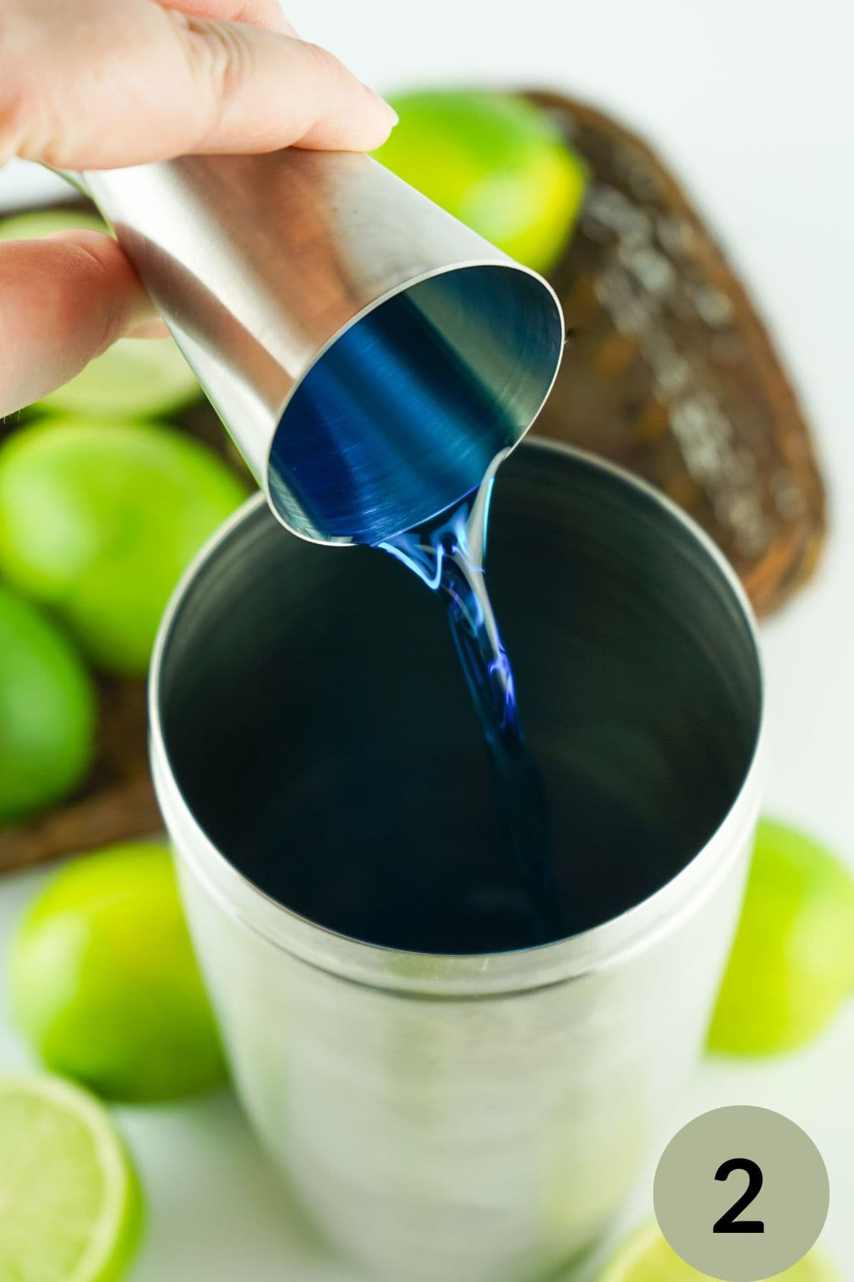 step 2 hand pouring blue curacao into a cocktail shaker