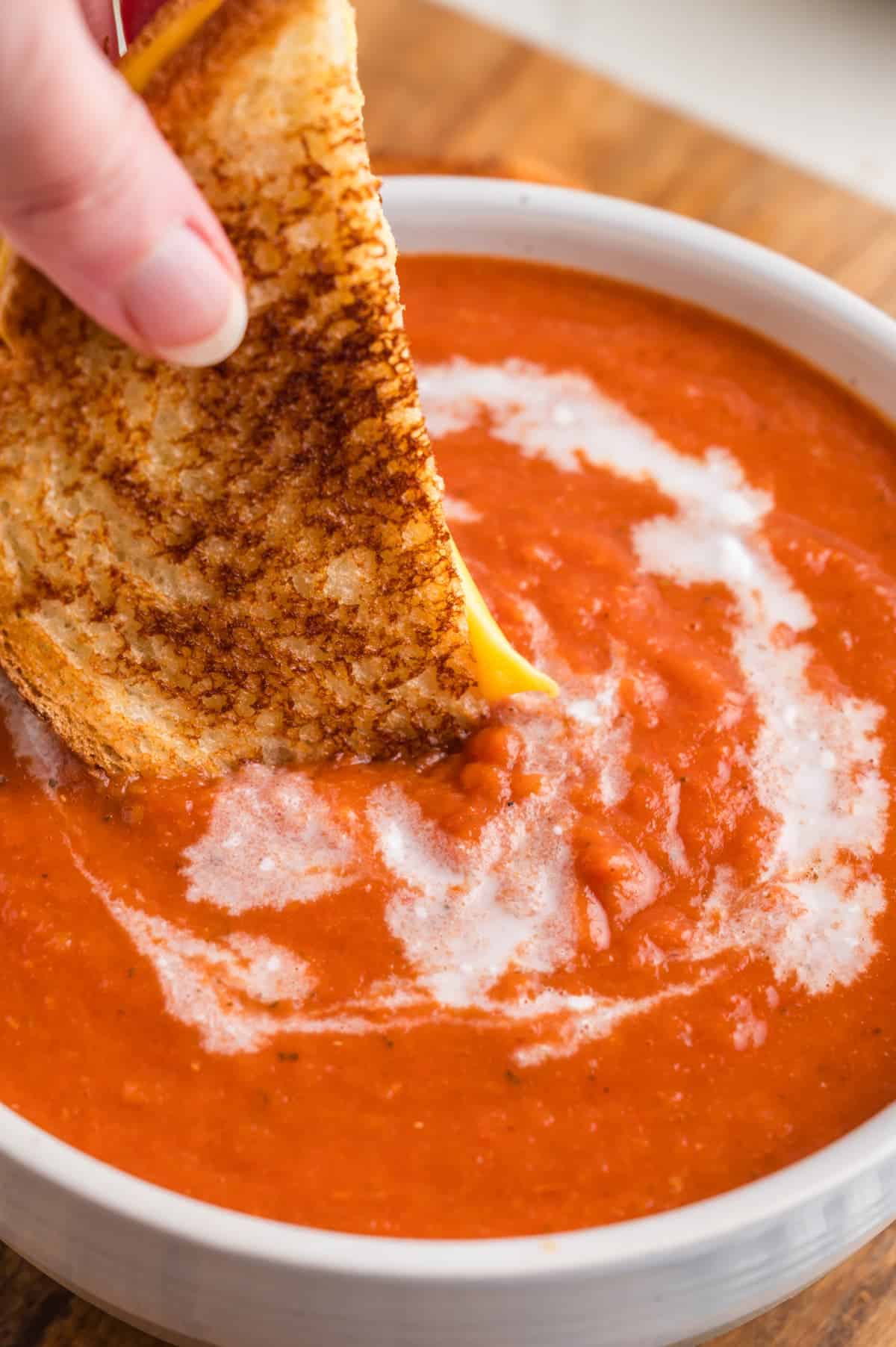 grilled cheese sandwich being dunked in a bowl of soup