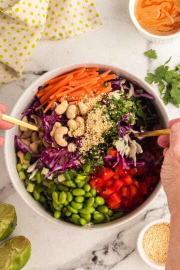 tossing the chopped thai salad with a serving fork and spoon