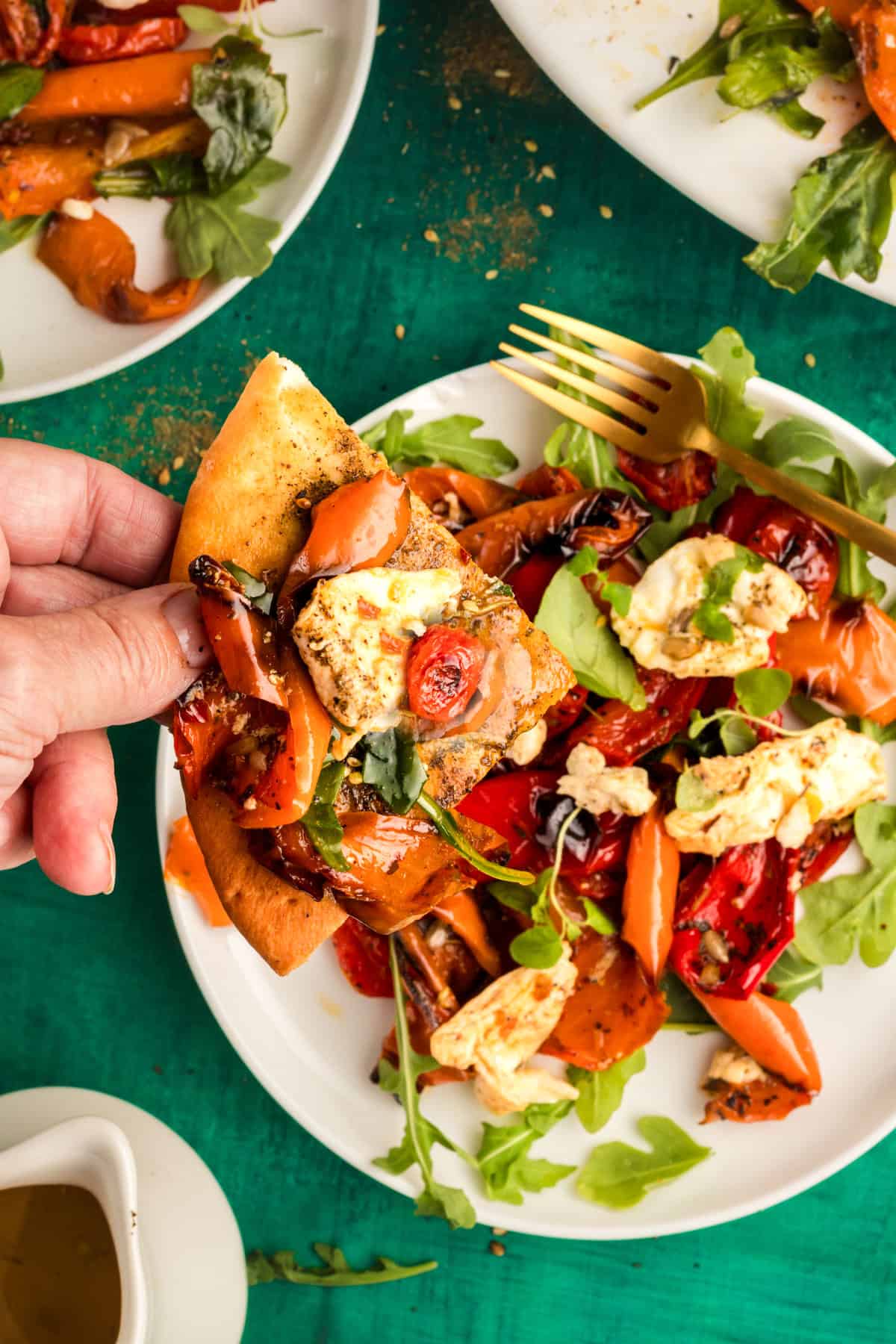 hand holding a piece of zaatar pita bread topped with bell pepper salad